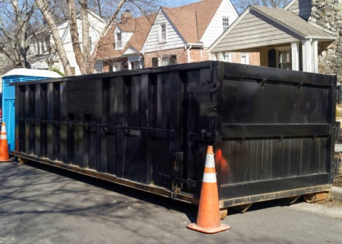 black industrial dumpster container on neighborhood street.